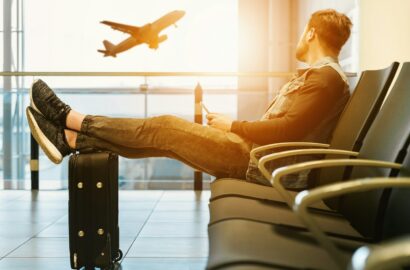 man sitting on gang chair with feet on luggage looking at airplane